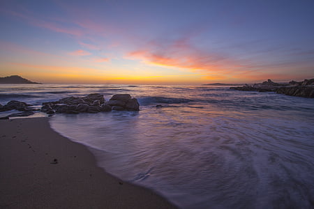 calm sea with rocks on seashore under orange sky thumbnail