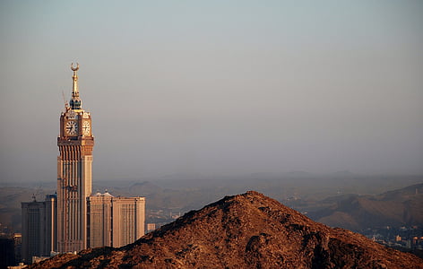 brown and gold tower clock surrounded with mountains thumbnail