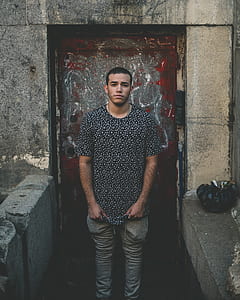 man wearing black t-shirt standing behind gray door thumbnail