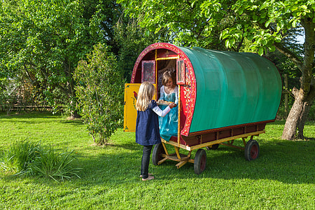 woman in blue dress passing tray to woman in teal dress inside wagon thumbnail