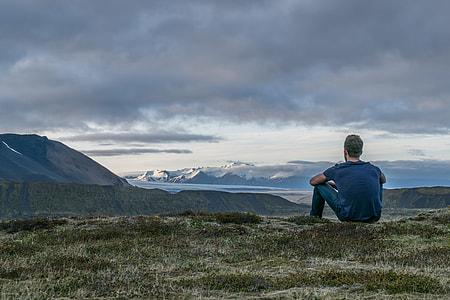 man sitting on green field while overlooking at mountains thumbnail