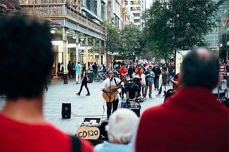 man holding acoustic guitar while singing on street surrounded by people thumbnail