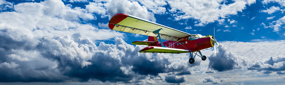yellow and red plane flying under white clouds thumbnail
