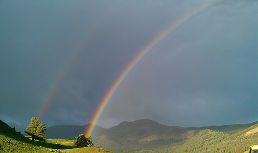 green mountain and trees with rainbow during daytime thumbnail