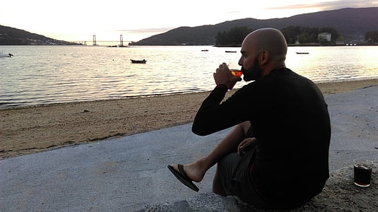 man sitting near shore while drinking thumbnail