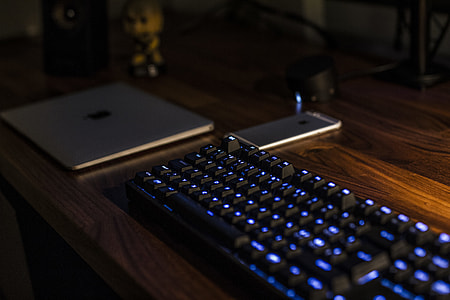 turned on mechanical keyboard beside MacBook and iPhone on table thumbnail