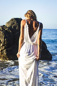 woman wearing white dress facing the sea with rock formation thumbnail