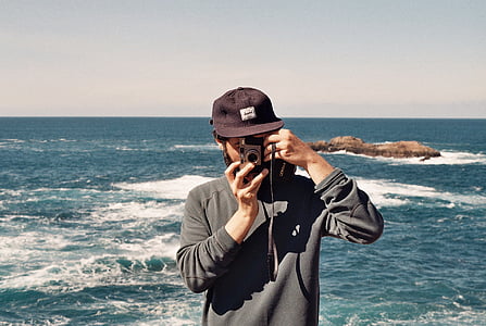 man taking photo with gray camera standing near body of water thumbnail