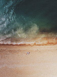 high-angle photography of person lying on beach blanket near body of water during daytime thumbnail