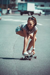 girl in white shirt and teal shorts riding skateboard at daytime thumbnail