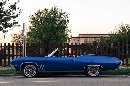 parked blue convertible hood car beside brown wooden fence thumbnail