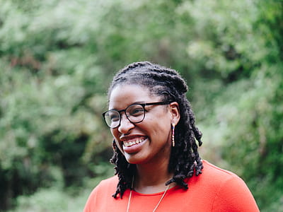 woman smiling while wearing black framed eyeglasses and orange scoop-neck top overlooking green leaf during daytime thumbnail