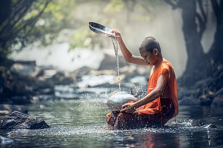 shallow focus photography of monk pouring water on silver pot at river thumbnail