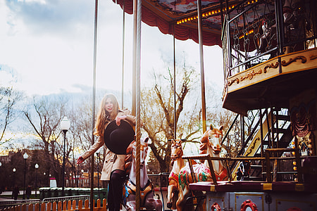 woman holding black sun hat while standing beside white horse carousel at daytime thumbnail