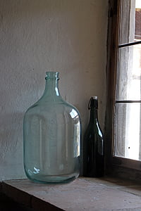 clear glass gallon and black glass bottle beside window thumbnail