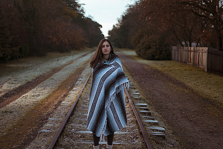 woman standing on train rail surrounded by trees during daytime thumbnail