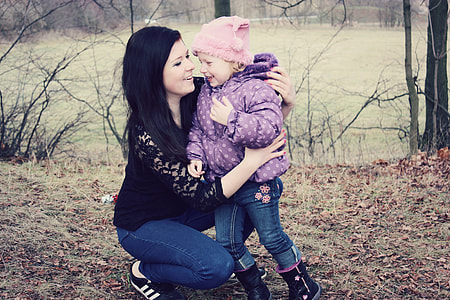 woman holding toddler near body of water during daytime thumbnail