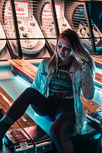 woman sitting on arcade machine inside dim-lighted room thumbnail