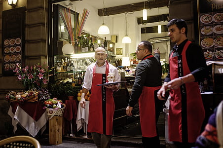 three men wearing red aprons standing inside black room thumbnail
