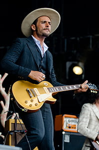 Man in Black and White Pinstripe Formal Coat and Pants Wearing Beige Hat Holding Brown Electric Guitar thumbnail
