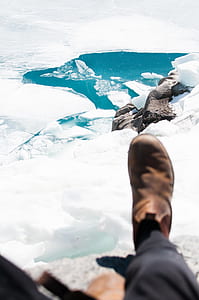person sitting on cliff near iceberg with calm body of water at daytime thumbnail