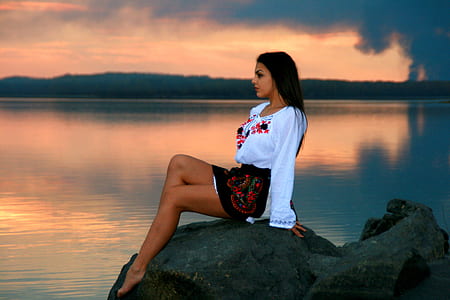 woman in white top sitting on rock near body of water thumbnail