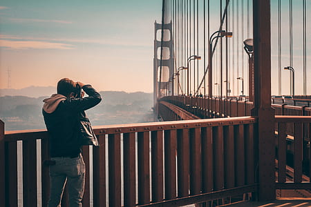 man wearing black leather jacket taking picture of bridge thumbnail
