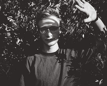 grayscale photography of man covering sunrays by left hand surrounded with leaves thumbnail