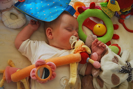 baby sleeping on white fabric sheet surrounded by toys thumbnail