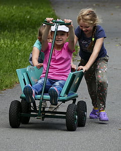 boy riding green push cart while girl pushing green cart behind at daytime thumbnail