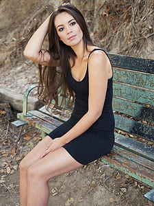 woman in black spaghetti-strap dress sitting on bench thumbnail