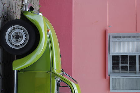 green Volkswagen New Beetle coupe parked beside pink concrete building thumbnail