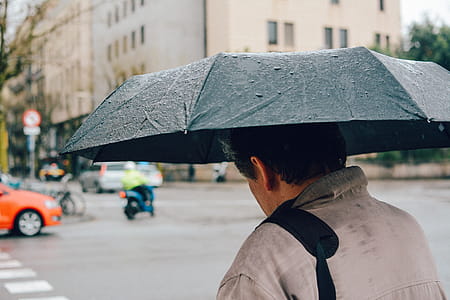 Man Holding Black Folding Umbrella Walking Along Street thumbnail