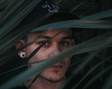 selective focus portrait photography of man wearing gauge earrings hiding at green leaves thumbnail