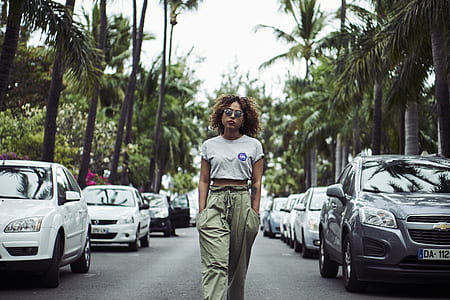 woman walking with hands in pocket between car parks and palm trees thumbnail