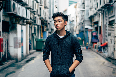 selective focus photography of man wearing black pullover hoodie holding pocket near houses thumbnail