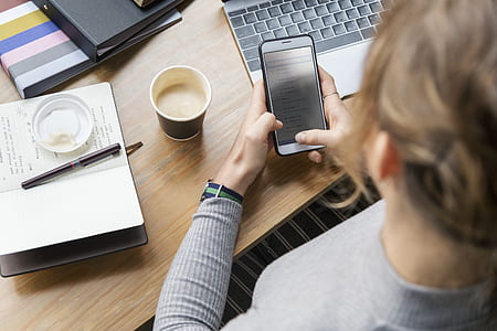 woman holding white smartphone beside grey laptop computer thumbnail