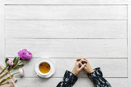 person leaning on beige wooden table beside white ceramic cup near purple petaled flower thumbnail