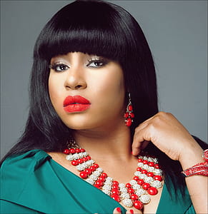 woman wearing blue shirt, red beaded bib necklace, red lipstick and dangling earrings thumbnail