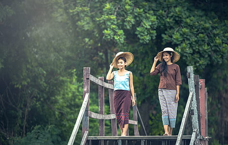 two women with hat walking on gray wooden bridge during daytime thumbnail