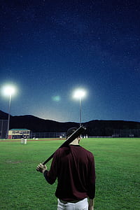 man holding baseball bat on baseball field during nighttime thumbnail