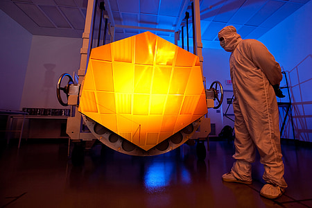 man wearing gray suit standing near hexagonal orange panel thumbnail