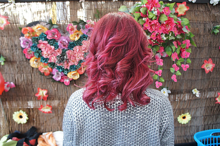 person with red hair wearing gray top facing wall with assorted petaled flowers thumbnail