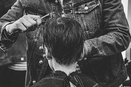 grayscale photo of man cutting boys hair thumbnail