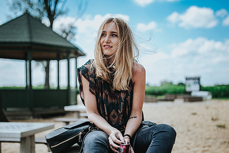 Beautiful blonde woman relaxing with a can of coke on a tree stump by the beach thumbnail