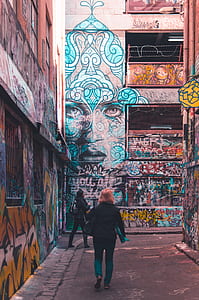 two women walking buildings with graffitis during daytime thumbnail
