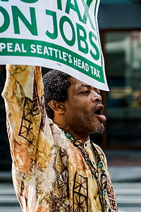 man holding green and white signage outdoors thumbnail