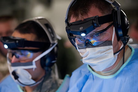 two men in blue lab gowns, face masks, and black-framed 3D glasses thumbnail