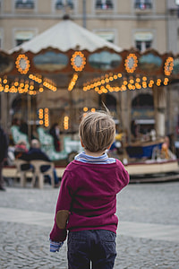 boy wearing blue polo shirt and red long-sleeved sweat shirt and black denim bottoms facing a turned on carousel during daytime thumbnail