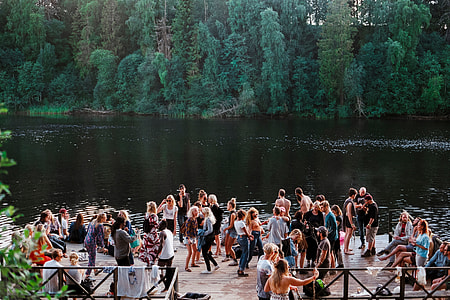 people gathered near lake surrounded by green trees thumbnail